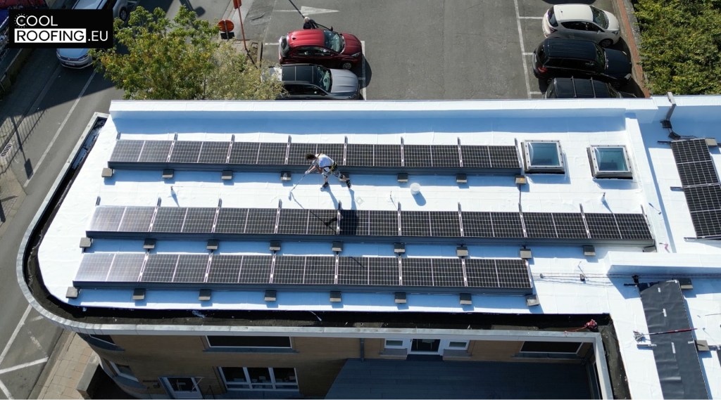 Application de peinture blanche sur la toiture d’une crèche communale à Wavre avec panneaux solaires pour limiter l’échauffement du bâtiment